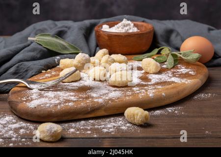 Kartoffel- und Mehlgnocchi, typisch italienische Pasta auf einem Holzschneidebrett mit Salbeiblättern Stockfoto