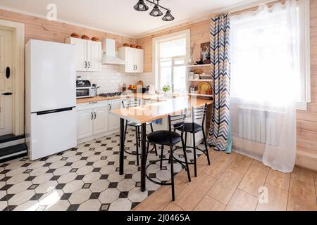 Moderne, weiße U-förmige Küche im skandinavischen Stil. In einem hellen rustikalen Haus, wo die Küche mit dem Wohnzimmer kombiniert wird Stockfoto