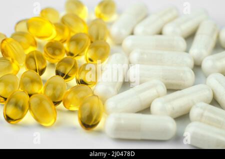 Pillen von zwei Arten Nahaufnahme. Gelbe Fischöl-Kapseln und weiße Vitamin-Komplex-Kapseln Stockfoto