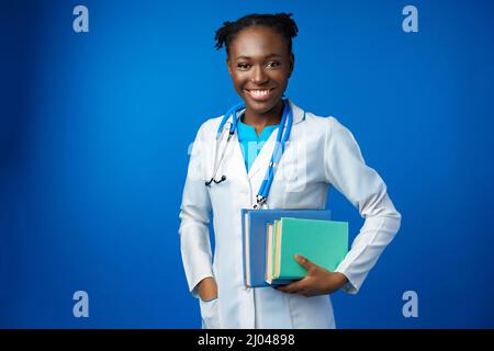 Schwarze Ärztin, die einen Laborkittel mit Buch trägt Stockfoto