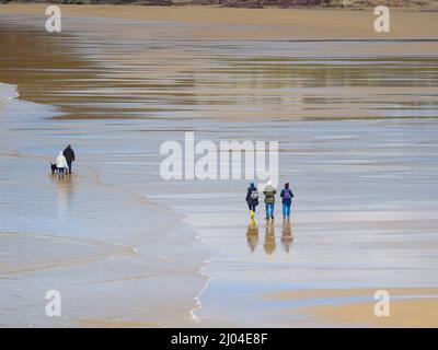 Menschen, die an einem kalten Frühlingstag am Polzeath Beach spazieren gehen, Cornwall, Großbritannien Stockfoto