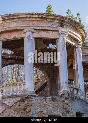 Verlassenes Restaurant im griechischen Stil mit kaputten Dach, leeren Fensteröffnungen und überwucherten Bäumen Stockfoto