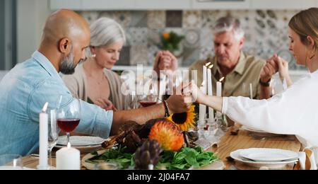 So dankbar für die Zeit, die wir zusammen verbringen können. Aufnahme von zwei Paaren, die sich zum Mittagessen hinsetzen und zu Hause beten. Stockfoto