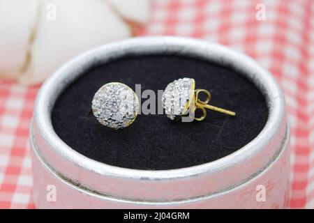 Schöne goldene Ohrringe mit Diamant-Display in Schmuckkachtel auf rotem karierten Tuch Hintergrund dekoriert Stockfoto