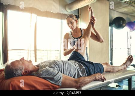 Unterstützung von Mitarbeitern bei der Maximierung ihrer Funktionsfähigkeit. Aufnahme eines älteren Mannes, der von einem Physiotherapeuten behandelt wurde. Stockfoto