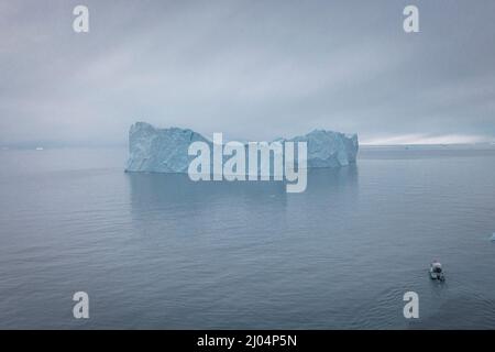 Kleines Boot, das aus der Luft vor extremen Eisbergen segelt Stockfoto