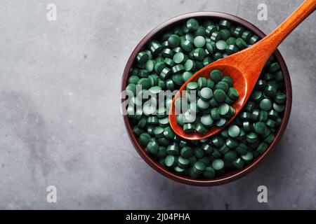 Spirulina-Tabletten aus kontrolliert biologischem Anbau in einem Holzbecher mit einem Holzlöffel auf einem dunklen Hintergrund mit freiem Raum Draufsicht Stockfoto