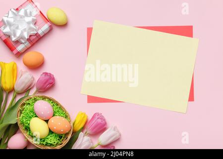 Osterkomposition. Geschenk Eier in Korb Blumen Tulpen leeren Blatt Papier mit Platz für Text auf rosa Hintergrund. Stockfoto