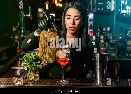 Die lateinamerikanische Brünette Kellnerin bereitet an der Bar einen Cocktail zu Stockfoto