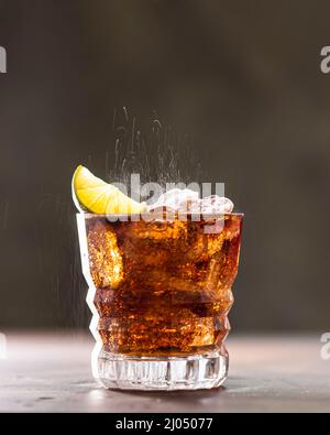 Cuba Libre mit braunem Rum, Cola, Minze und Limette. Kaltes Longdrink, alkoholischer Cocktail. Platz für Text, dunkler Hintergrund. Stockfoto