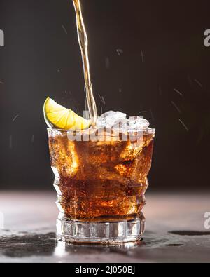 Cuba Libre mit braunem Rum, Cola, Minze und Limette. Kaltes Longdrink, alkoholischer Cocktail. Platz für Text, dunkler Hintergrund. Stockfoto