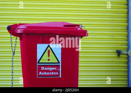 Roter Behälter für die Sammlung von Asbestabfällen, gekennzeichnet mit Warnschild Stockfoto