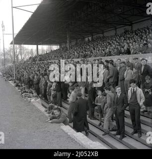 1960s, historische Fußballfans, die auf Betonterrasen auf der unteren Ebene der Haupttribüne auf dem Manor Ground stehen, dem Heimstadion des Fußballclubs Oxford United von 1925 bis 2001. Der Verein wurde 1893 als Headington gegründet, 1911 wurde die Endung United hinzugefügt. Der Name Oxford United wurde 1960 angenommen. Stockfoto