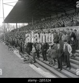 1960s, historische Fußballfans, die auf Betonterrasen auf der unteren Ebene der Haupttribüne auf dem Manor Ground stehen, dem Heimstadion des Fußballclubs Oxford United von 1925 bis 2001. Der Verein wurde 1893 als Headington gegründet, 1911 wurde die Endung United hinzugefügt. Der Name Oxford United wurde 1960 angenommen. Stockfoto