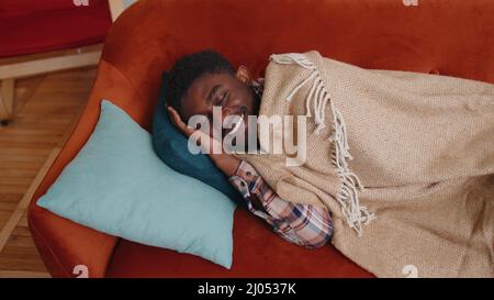 afroamerikanischer junger Mann, der zu Hause ruhig im Schlafzimmer schläft, lächelt und auf einem bequemen Bett liegt Stockfoto