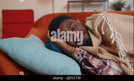 afroamerikanischer junger Mann, der zu Hause ruhig im Schlafzimmer schläft, lächelt und auf einem bequemen Bett liegt Stockfoto