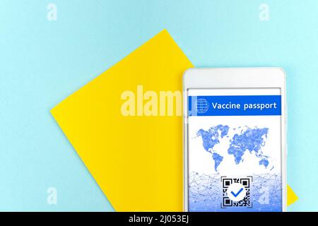 Gelb ein Blatt Papier mit Smartphone, das einen gültigen digitalen Impfpass QR-Code für COVID-19 auf blauem Hintergrund anzeigt Stockfoto