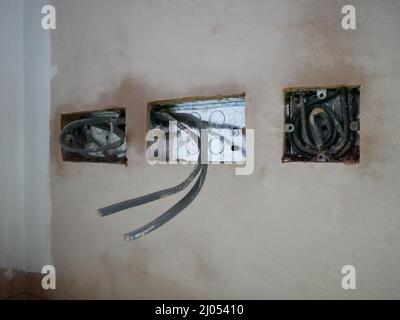 Befestigen Sie zuerst Steckdosen für Elektroinstallationen in einer frisch verputzten Wand. Stockfoto