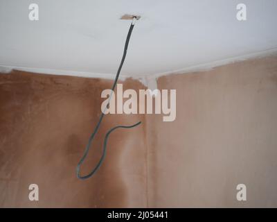 Befestigen Sie zunächst Elektrokabel in einer frisch verputzten Wand. Stockfoto