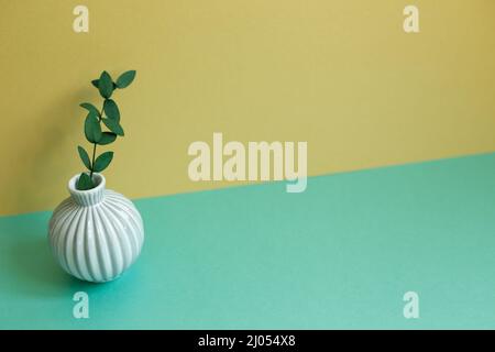 Vase aus grünem Eukalyptusblatt auf grünem Tisch. Gelber Wandhintergrund Stockfoto