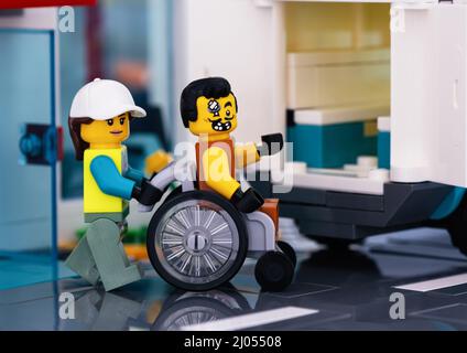 Tambow, Russische Föderation - 11. Februar 2022 Ein Lego-Sanitäter-Minifigur, der einen Rollstuhl schiebt, während ein Lego-Patient darin sitzt Stockfoto