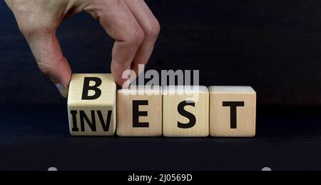 Symbol für beste Investition. Geschäftsmann dreht einen Holzwürfel und ändert das Wort Invest in Best. Schöner grauer Tisch, grauer Hintergrund. Business und Best Inve Stockfoto