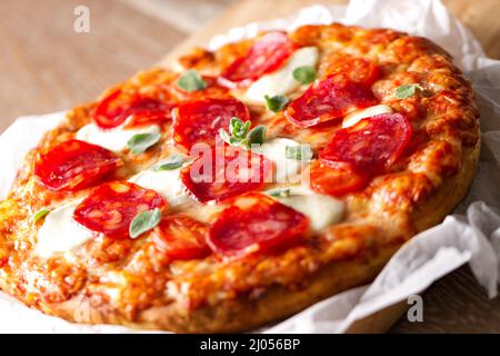 Pizza mit Pfefferoni-Wurst und Käse auf einem Holzbrett auf einem Holzhintergrund Stockfoto
