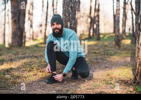 Der junge sportliche Mann bindet Schuhe in die Natur. Stockfoto