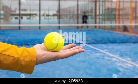 Männliche Hand hält Paddel-Tennisball. Starteinstellung des professionellen Players. Männer spielen ein Match im Freien. Mann spielt Padel auf einem Blue Grass Court outdo Stockfoto