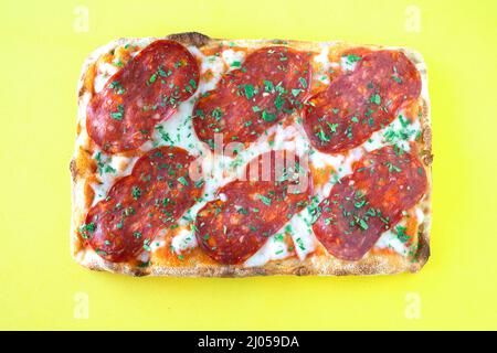 Salami Pizza al Taglio isoliert auf gelbem BGD Stockfoto