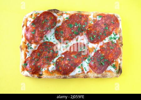 Salami Pizza al Taglio isoliert auf gelbem BGD Stockfoto