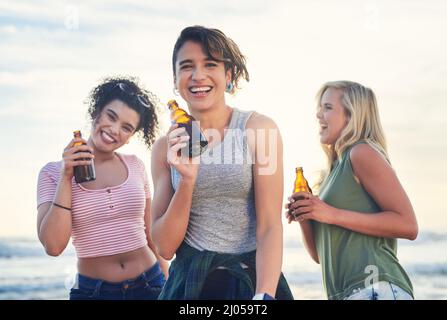 Wir bringen die Party überall hin. Aufnahme von drei Freunden, die am Strand einen Drink genießen. Stockfoto
