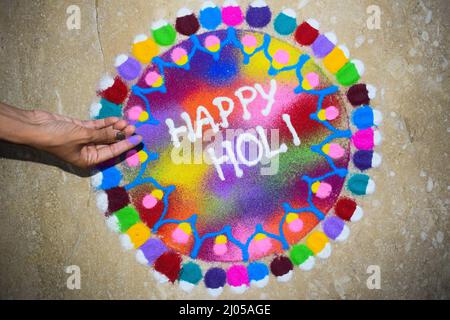 Weibliche Herstellung schöne und bunte Happy Holi rangoli zu Hause während Holi Festival gemacht. Holi Feiern im Haus mit Rangoli bunten Pulver. r Stockfoto