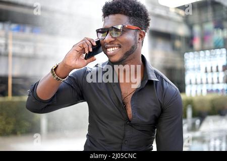 Afrikanischer stilvoller Mann im Gespräch mit dem Handy, während er im Freien lächelt Stockfoto
