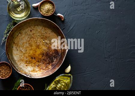 Leere alte Bratpfanne, umgeben von Gewürzen auf dunklem Hintergrund. Für Text platzieren. Kochkonzept. Stockfoto