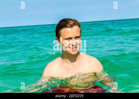 hübscher Teen hat Spaß Schwimmen im Ozean unter blauem Himmel Stockfoto