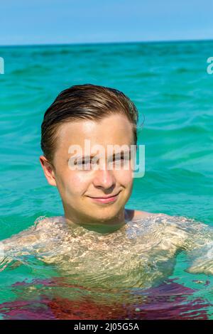 hübscher Teen hat Spaß Schwimmen im Ozean unter blauem Himmel Stockfoto