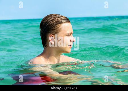 hübscher Teen hat Spaß Schwimmen im Ozean unter blauem Himmel Stockfoto