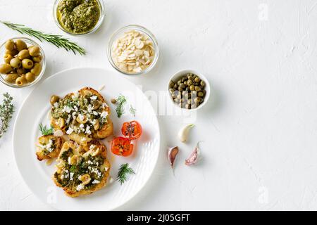 Blumenkohlesteak mit Gewürzen, Chimichurri-Sauce, Mandelflocken, Oliven, gebratenen Kirschtomaten und Kapern auf einem weißen Teller. Vegetarische Gerichte. Stockfoto