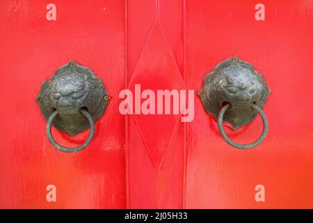 Atemberaubende rote Holztür im thailändischen Stil mit bronzenem Löwenknocker eines historischen Gebäudes, das von König Rama V, Bangkok, Thailand, erbaut wurde Stockfoto