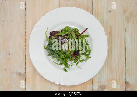 Salat aus Rucola-Spinat und Rübenwurzelblättern auf einem weißen Teller Stockfoto