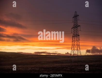 Lauder Moor, Scottish Borders, Großbritannien. 15. März 2022. Ein Blick auf den Sonnenuntergang über einem Strompylon, da die Energiepreise voraussichtlich weiter steigen werden. Quelle: phil wilkinson/Alamy Live News Stockfoto