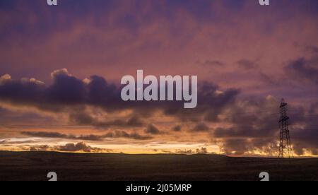 Lauder Moor, Scottish Borders, Großbritannien. 15. März 2022. Ein Blick auf den Sonnenuntergang über einem Strompylon, da die Energiepreise voraussichtlich weiter steigen werden. Quelle: phil wilkinson/Alamy Live News Stockfoto