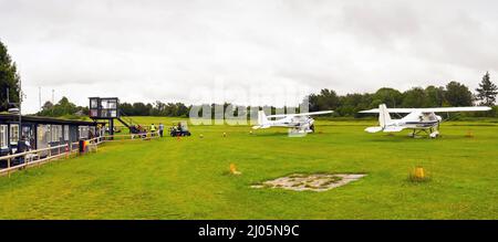 Popham, bei Basingstoke, England - August 2021: Kleines Leichtflugzeug, das vor den Gebäuden und dem Kontrollturm des Flugplatzes Popham geparkt ist. Stockfoto