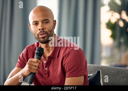 Ich habe einige Worte der Weisheit für Euch. Ausgeschnittene Aufnahme eines jungen Mannes, der auf einem Sofa sitzt, während er über ein Mikrofon spricht. Stockfoto