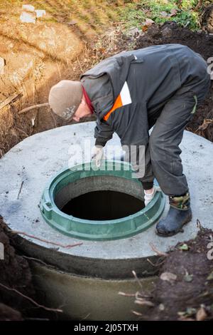 Ein Arbeiter installiert einen Schachtler auf einem Klärgruben. Kommunikation in einem Wohngebäude. Stockfoto