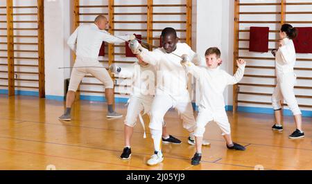 Fokussierte fleißige Jungen fechten aufmerksam zu professionellen effizienten freundlichen Fechttrainer im Fitnessstudio hören Stockfoto