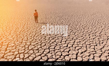Silhouette eines Mannes auf einem sandigen geknackten leeren, nicht fruchtbaren Land während einer Dürre. Das Konzept der ökologischen Katastrophe auf dem Planeten. Sonniger Tag Stockfoto