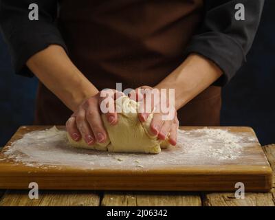 Die Hände des Küchenchefs kneten den Teig auf einem Holzbrett. Makroaufnahme. Zubereitung von Teigprodukten. Rezepte für Pizza, Brot, Pasta, Gebäck. Home Co Stockfoto
