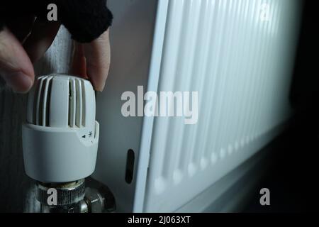 Steigende Heizkosten - Eine Handschuhen greift nach dem Zifferblatt auf einem Heizkörper Stockfoto